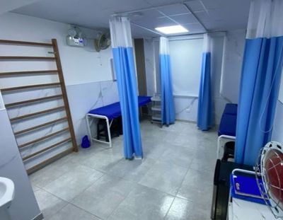 Sala de camillas de Rehabilitación Las Lomas: dos camillas azules separadas por cortinas azules, con una espaldera de madera a un lado.
