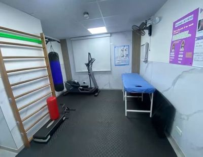 Sala de equipos con piso de tatami negro: espaldera de madera, bicicleta elíptica, saco de boxeo colgante, step y una camilla azul.